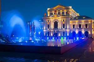Mehedinti chargers Night photo of an old building with a blue lighted fountain in front.