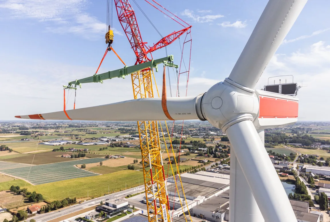 Crane lifting a blade onto a wind turbine during installation.